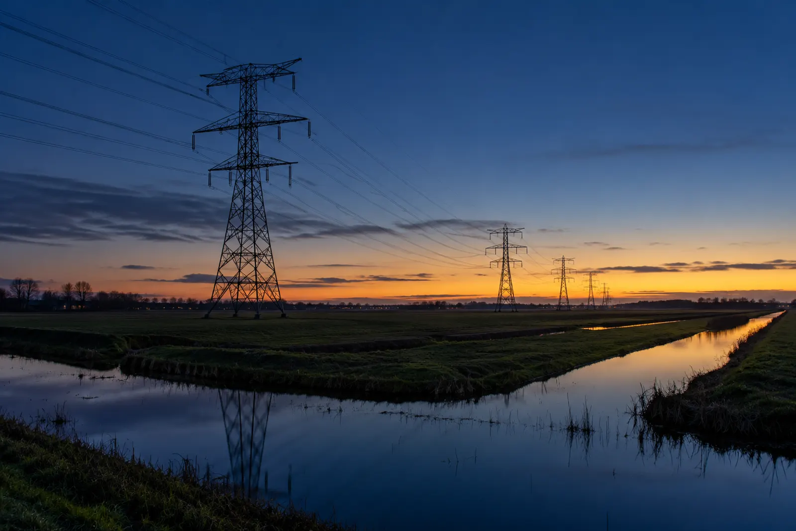 Hoogspanningsmasten in een polder bij schemering